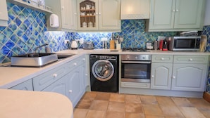A compact kitchen with a washing machine, oven, and microwave. - Waterhead Cottage (Windermere)