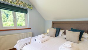 A neatly made bed with pillows and folded towels, a window with a view of greenery, and a radiator below. - Waterhead Cottage (Windermere)