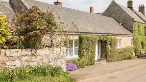 A stone cottage with a sloped roof, ivy-covered walls, and a stone wall in front.