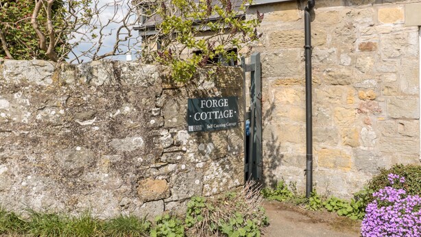 A stone cottage with a sign reading "Forge Cottage Self Catering Cottage."