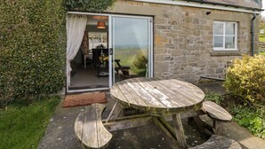 A stone house with a wooden table and benches outside.