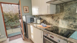 A compact kitchen with a refrigerator, microwave, toaster, and oven. A wooden cutting board with a cup and saucer is on the counter.