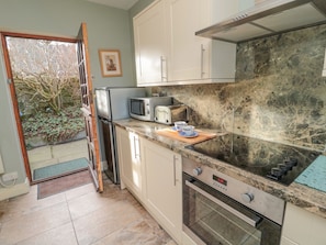 A compact kitchen with a refrigerator, microwave, toaster, and oven. A wooden cutting board with a cup and saucer is on the counter.