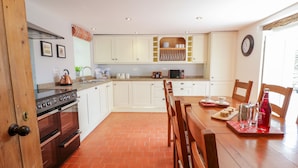 A kitchen with white cabinets, a stove, and a dining table with chairs. - Tai Ucha (Corwen)