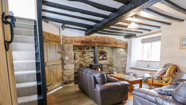 A cozy living room with a stone fireplace, leather sofas, a wooden coffee table, and a staircase leading to an upper level. - Tai Ucha (Corwen)