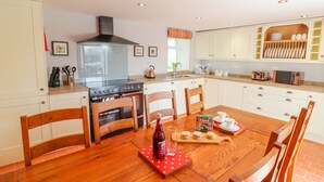 A kitchen with white cabinets, a stove, and a dining table with chairs. - Tai Ucha (Corwen)