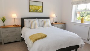 Quarto bem arrumado com uma cama, duas mesas de cabeceira, um criado-mudo, uma janela com vista e um quadro na parede.