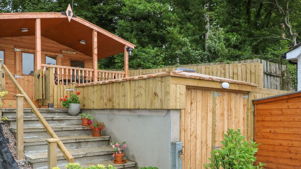 A wooden deck with a covered porch, stone steps, and potted plants. - Quiet Waters Cottage (Coleraine)