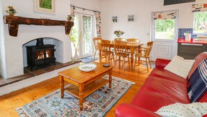 A cozy living room with a fireplace, wooden furniture, and a red sofa. - Quiet Waters Cottage (Coleraine)