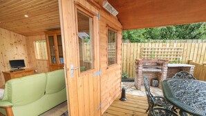 A wooden cabin with a green sofa, a dining table with metal chairs, and a barbecue grill outside. - Quiet Waters Cottage (Coleraine)