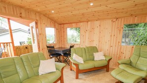 A wooden cabin interior with green leather sofas, a dining table, and chairs. - Quiet Waters Cottage (Coleraine)