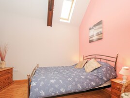 Un dormitorio con cama, cómoda de madera, mesita de noche y una pequeña mesa con lámpara.