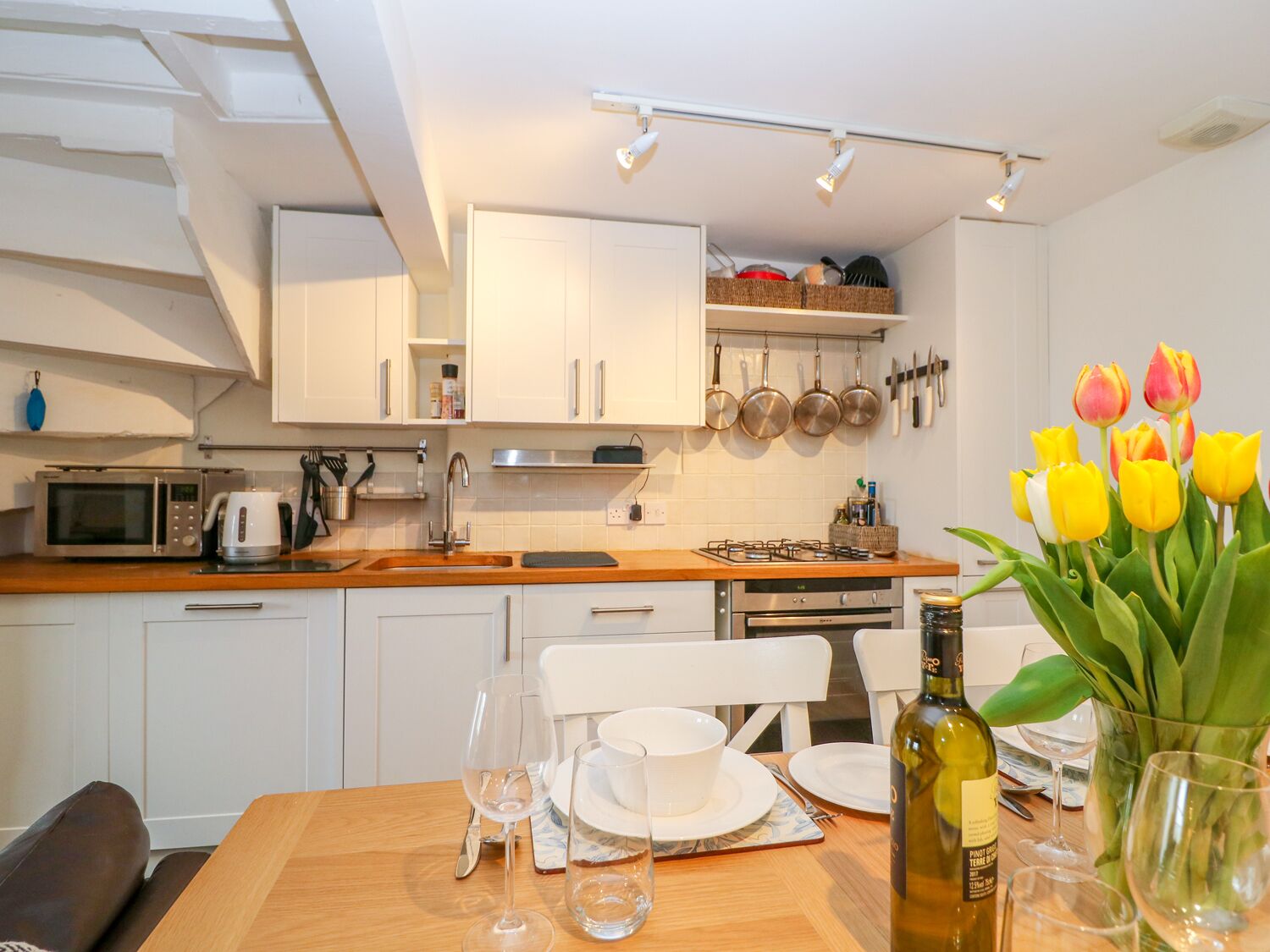 A modern kitchen with white cabinets, a wooden countertop, and a dining area with a table set for two.