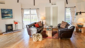 Ein gemütliches Wohnzimmer mit Holzboden, zwei Ledersofas mit Kissen, einem kleinen Holztisch, einem flauschigen Teppich, einem Kamin und einem Bild an der Wand.