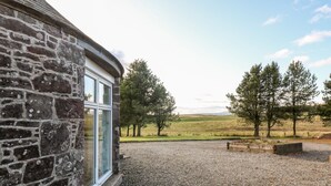 Ein Steinhaus mit Kiesweg und Blick auf ein grasbewachsenes Feld mit Bäumen.