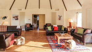 Ein geräumiges Wohnzimmer mit hoher Decke, Holzbalken und einem großen Fenster. Es gibt zwei Sofas, einen Couchtisch und einen Teppich.