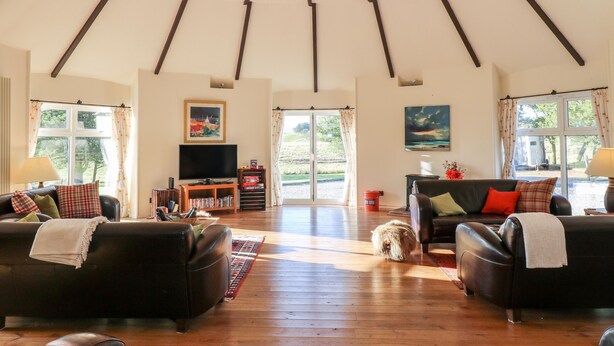 Ein geräumiges Wohnzimmer mit hoher Decke, Holzbalken, einem Fernseher und zwei Sofas.