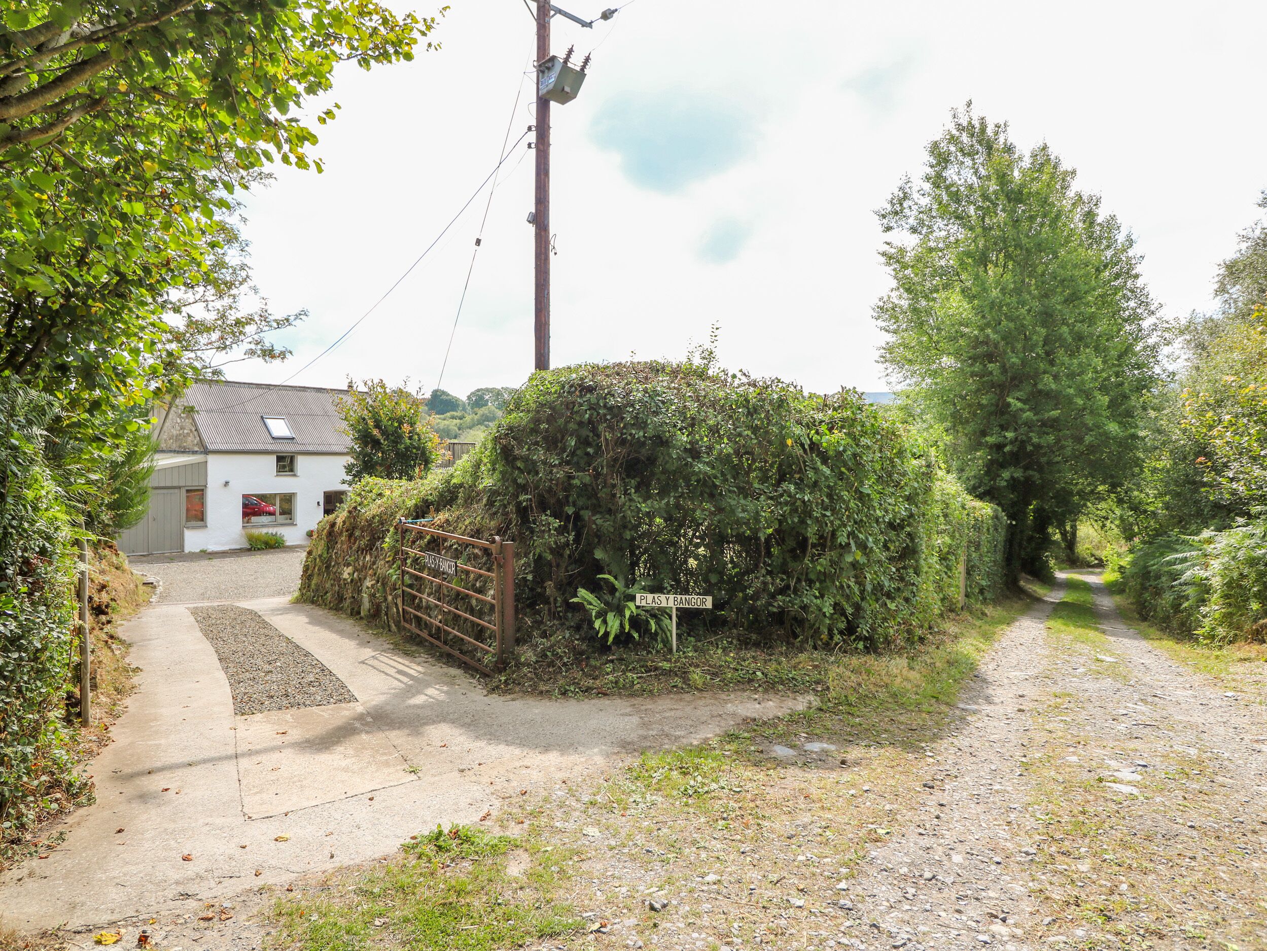 A rural road leading to a white house with a gravel driveway and a metal gate.
