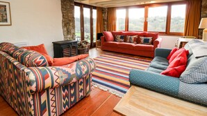 Una sala de estar acogedora con un sofá estampado, un sofá rojo y un sofá azul con cojines rojos. Hay una mesa de centro de madera y una chimenea con leña.