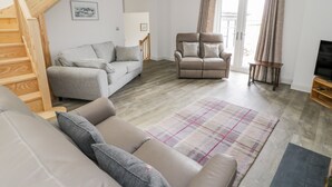Ett rymligt vardagsrum med en grå soffa, en beige fåtölj och en trätrappa.