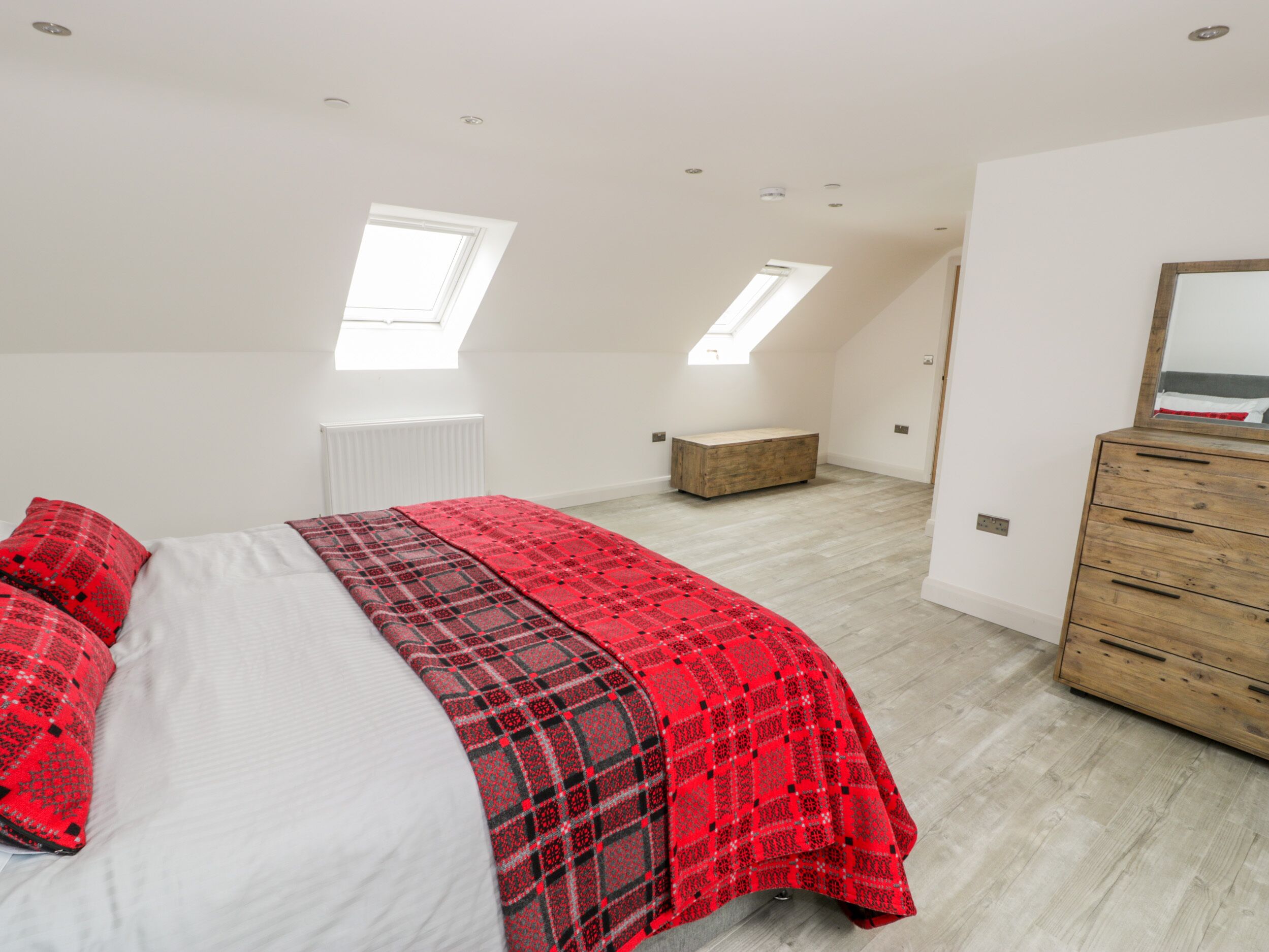 A bedroom with a bed, a dresser, and two skylights.