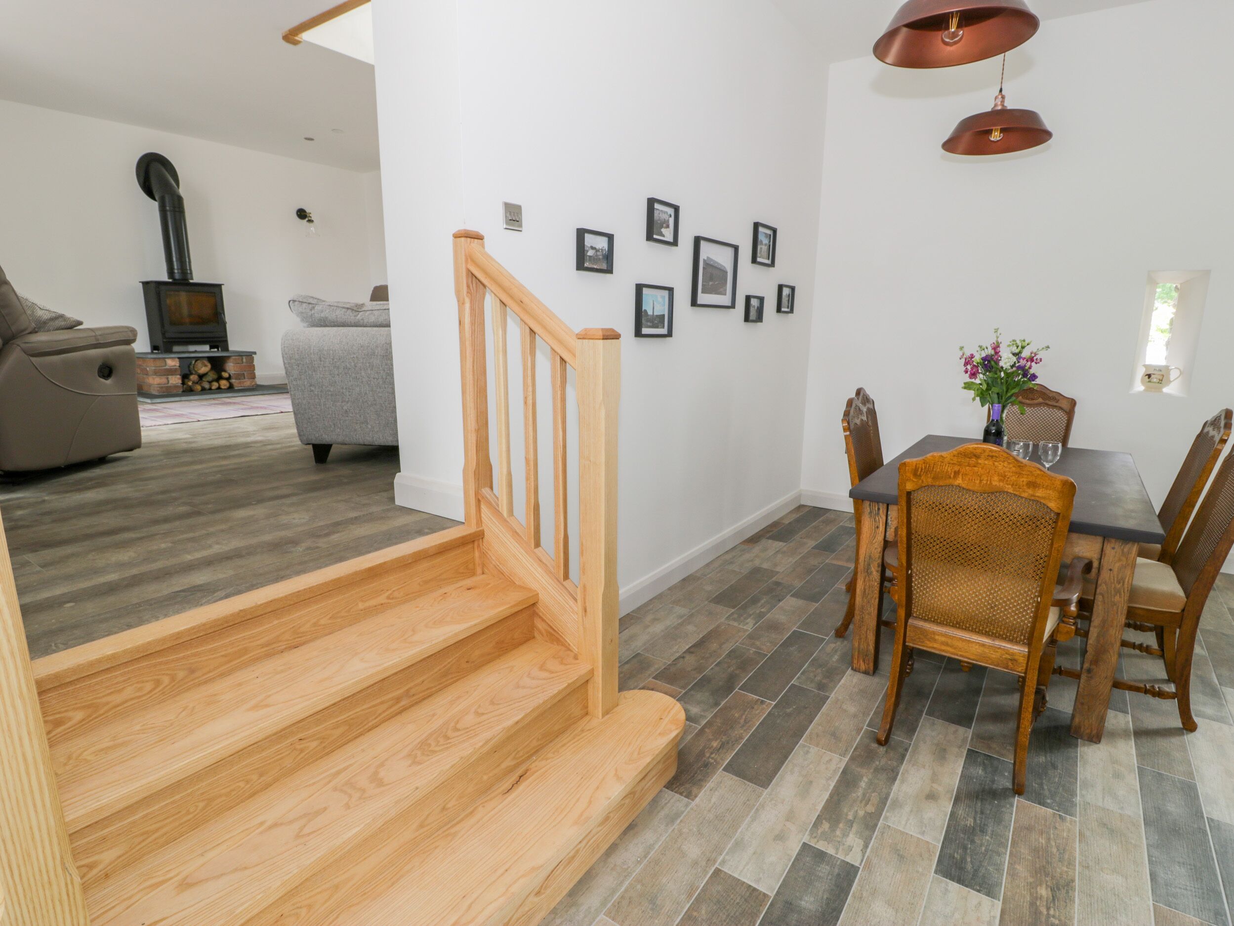 A modern living room with a fireplace, a dining area with wooden furniture, and a staircase.