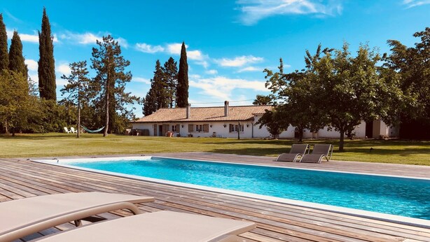 Una terraza de madera con piscina, sillones de descanso y una casa al fondo.