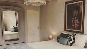 Un dormitorio con una cama grande, un espejo, un cuadro y una lámpara de mimbre.