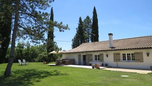 Una casa de dos plantas con techo de tejas, un patio con mobiliario exterior y un césped.