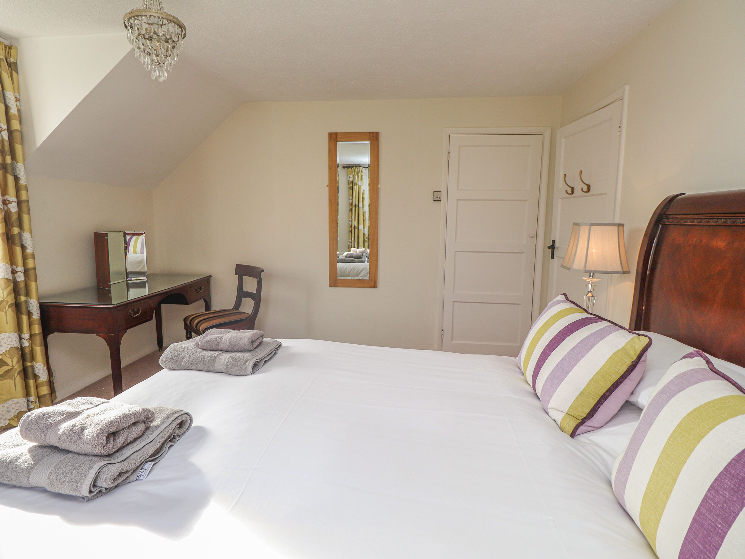Een hotelkamer met een bed, bureau, stoel, spiegel en deur.