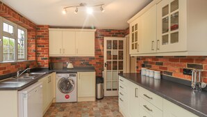 A compact kitchen with a washing machine, a sink, and a stove. - Knights Cottage (Maidstone)
