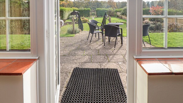 A view through a window of a patio area with a stone floor, outdoor furniture, and a garden. - Knights Cottage (Maidstone)