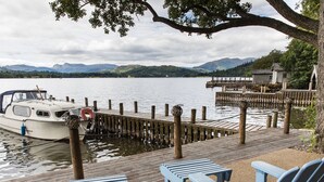 A dock with a boat, wooden deck, and Adirondack chairs. - Lakeside Cottage (Windermere)