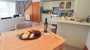 A dining area with a table set for a meal, a kitchen with light-colored cabinets, and a staircase leading to another level. - Lakeside Cottage (Windermere)
