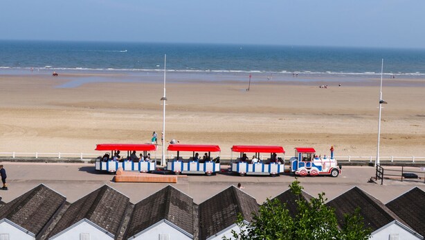 Vista de la playa con una hilera de vehículos tipo beach buggy de techo rojo, azul y blanco estacionados a lo largo de la orilla.