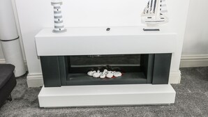 Una chimenea moderna con un faldón blanco, dos modelos decorativos de barcos y una colección de piedras blancas.