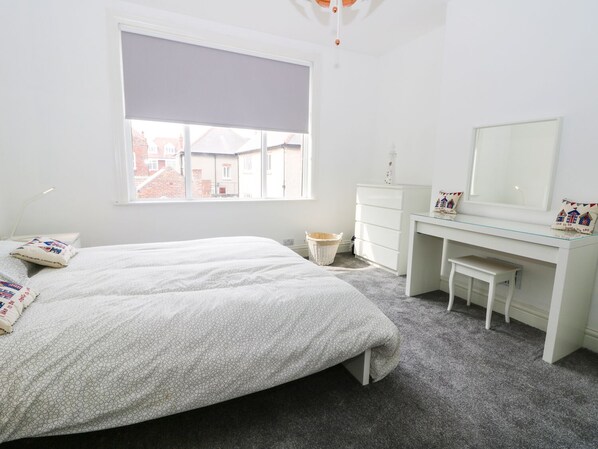 A bedroom with a bed, a desk, a chair, a window, and a dresser.