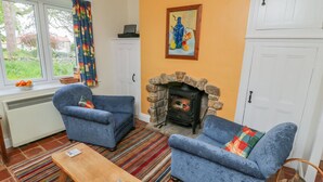A cozy living room with two blue armchairs, a wooden coffee table, a stone fireplace, and a colorful striped rug. - Manor Cottage (Pickering)