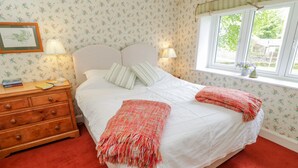 A bedroom with a bed, two bedside lamps, a wooden dresser, and a window with a view. - Manor Cottage (Pickering)