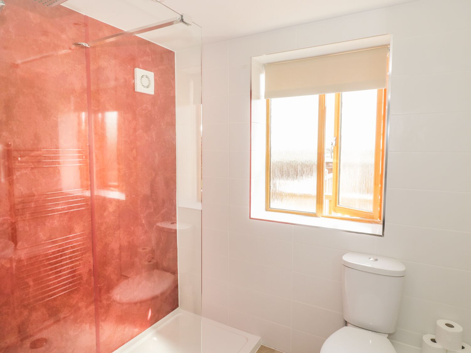 Une salle de bain avec une douche à parois de verre, des toilettes et une fenêtre donnant sur un paysage agréable.