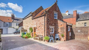 A brick house with a tiled roof, a front door, and a small porch with outdoor furniture and potted plants. - Moor Croft (Whitby)