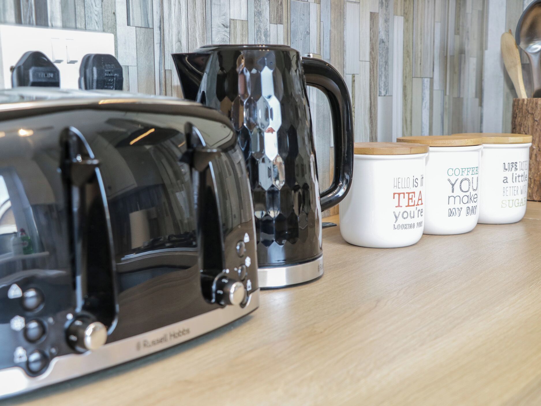 Un plan de travail de cuisine avec un grille-pain, une bouilloire et trois tasses à café ornées de citations inspirantes.
