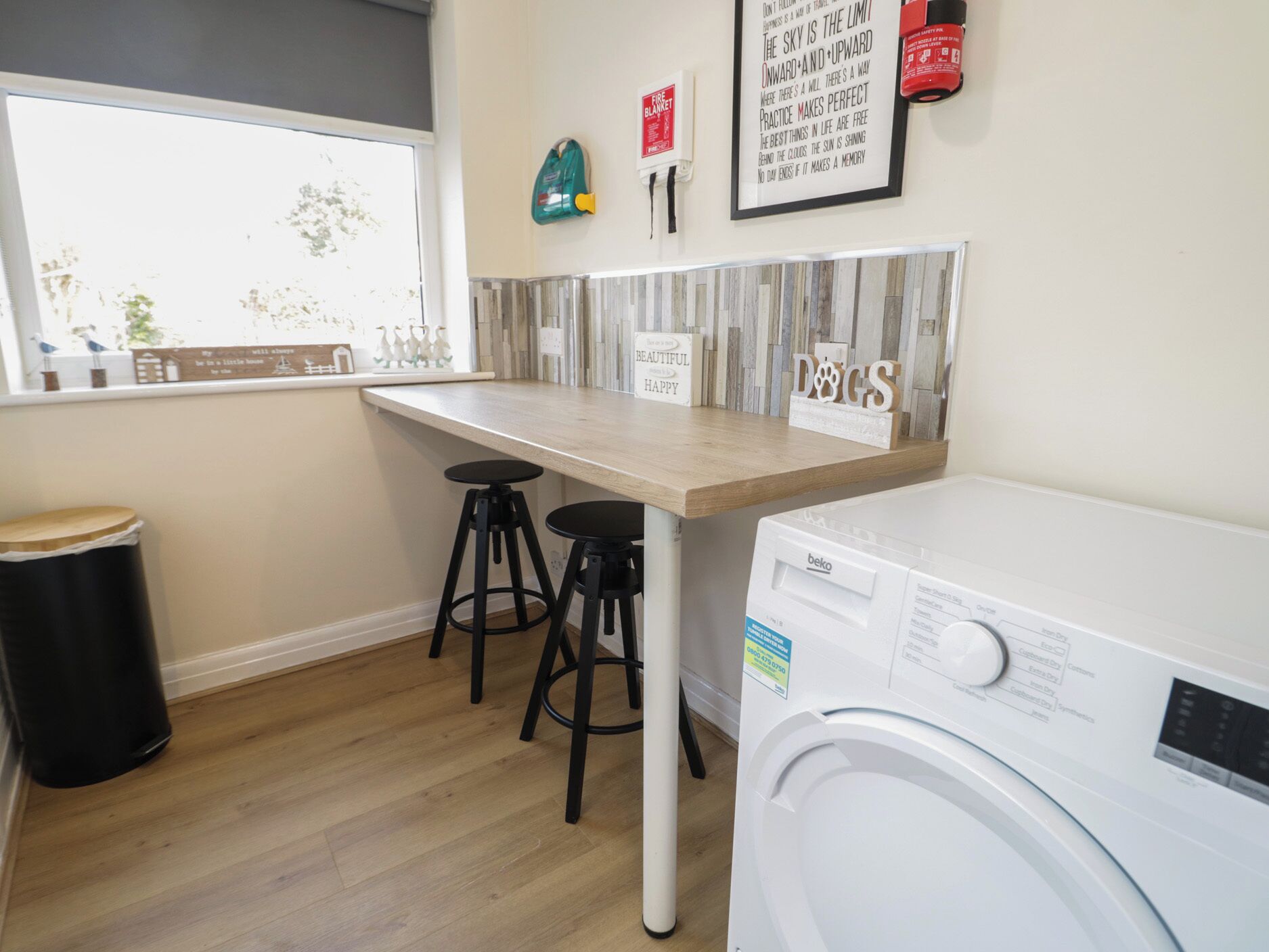 A laundry room with a washing machine, two stools, a window, and motivational wall art.