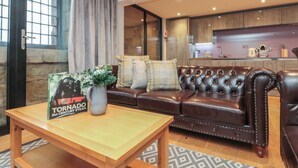 A modern living room with a leather sofa, a wooden coffee table, and a kitchen in the background. - Tornado @ Engine Shed (Whitby)
