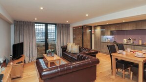A modern living room with a leather sofa, a TV, and a dining area with a table and chairs. - Tornado @ Engine Shed (Whitby)