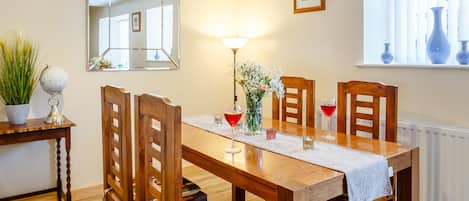 A dining room with a wooden table, chairs, a mirror, a lamp, and a window with curtains.
