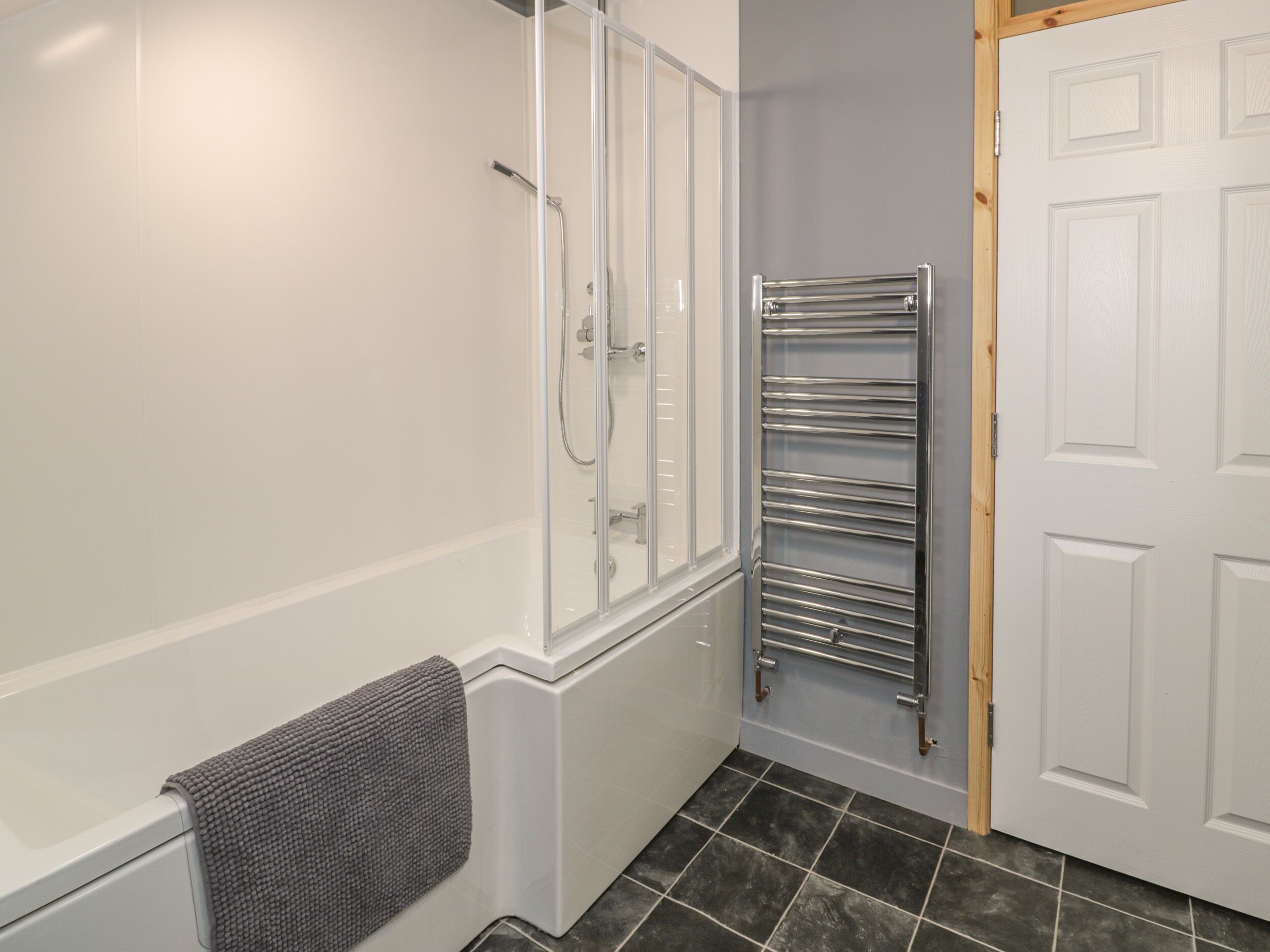 A bathroom with a shower, a towel rack, and a door.