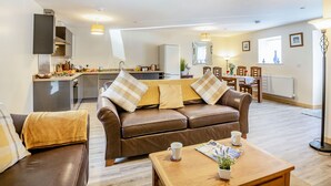 Ein modernes Wohnzimmer mit einem braunen Ledersofa, einem Holztisch und einem Essbereich im Hintergrund.