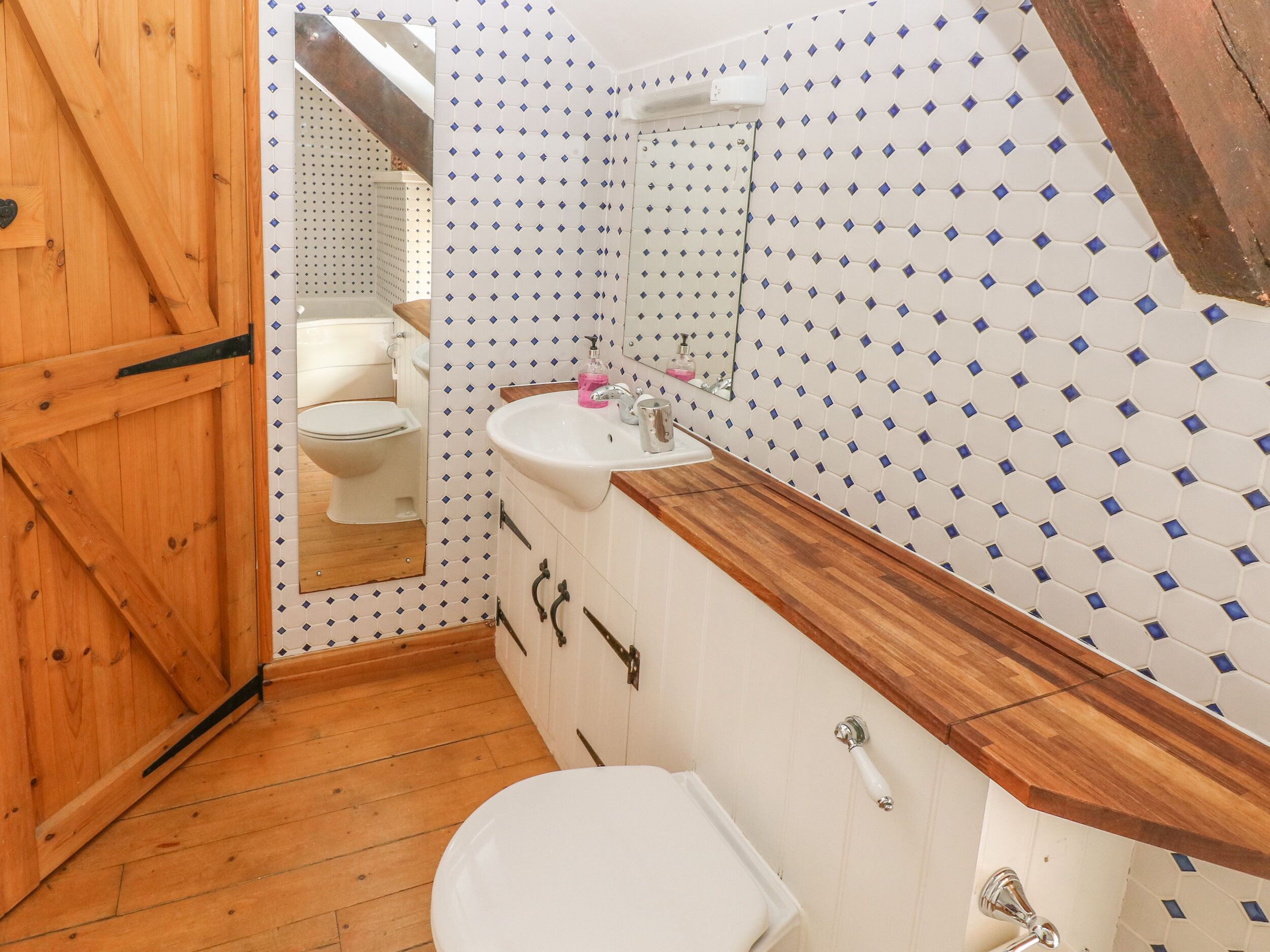 A bathroom with a wooden floor, white toilet, and a sink with a wooden countertop.