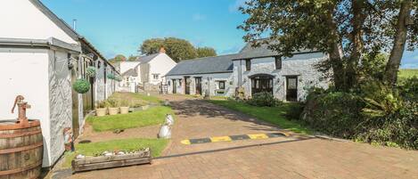 A rural village with stone buildings, a paved road, and a grassy area with a barrel.